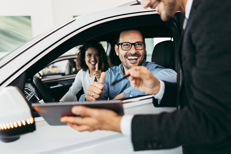 A smiling man in a car going over paperwork with a salesperson.